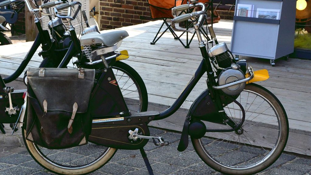 Deux VéloSolex noirs avec sacoches de cuir, garés sur une terrasse
