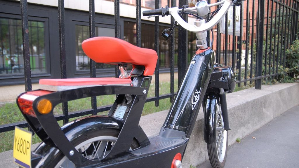 Solex à selle rouge et plaque d'immatriculation jaune, garé contre une grille