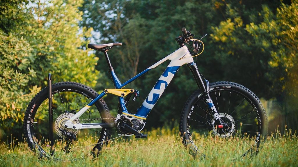 VTT à assistance électrique blanc et bleu posé dans l'herbe, en lisière de forêt