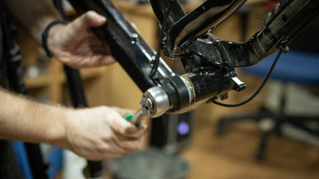 Mains qui serrent une vis au niveau du moteur d'un cadre de vélo électrique, dans un atelier