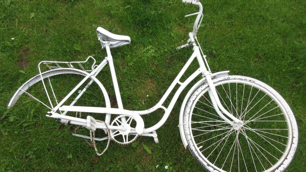 Vélo ancien blanc à cadre repeint posé dans l'herbe