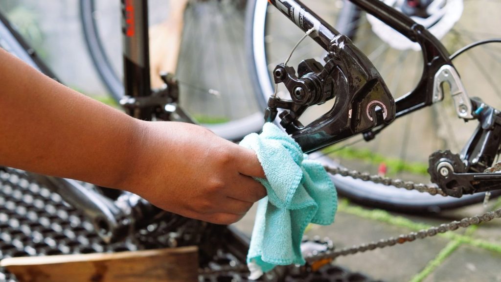 Main qui nettoie la chaîne et le dérailleur d'un vélo avec un chiffon