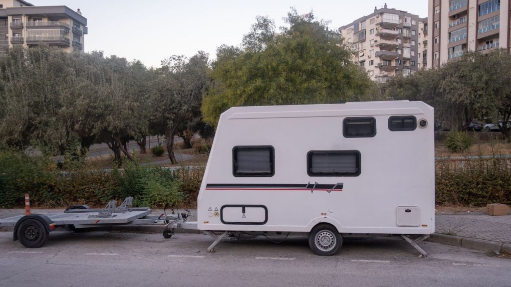 Caravane blanche stationnée le long d'une rue, avec sa barre d'attelage à l'avant